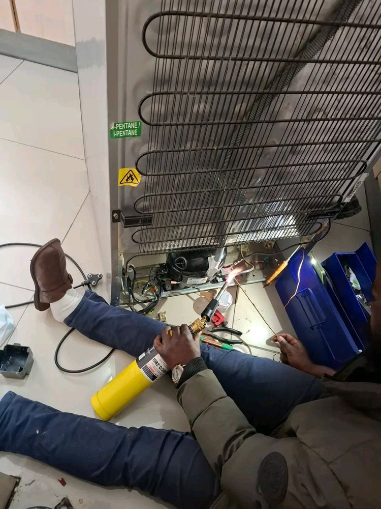 Technician brazing a copper pipe on the back of a fridge